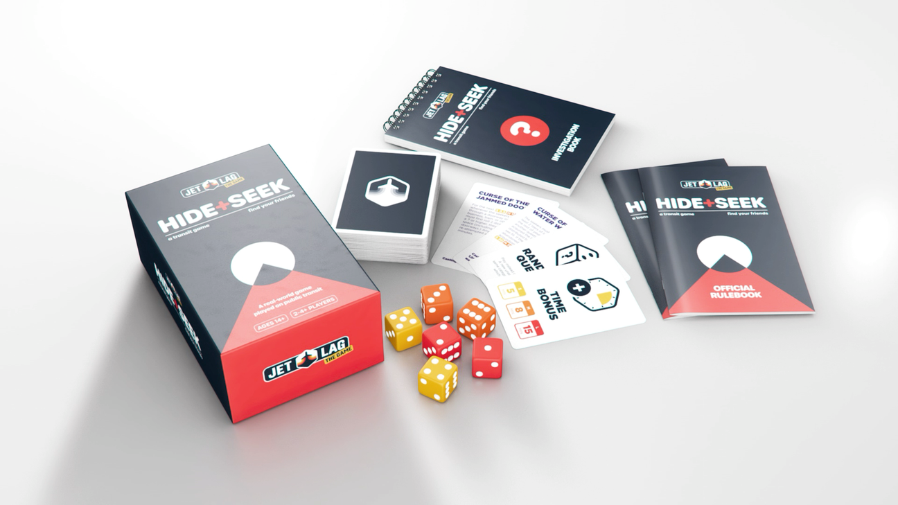 A promotional image of Jet Lag: The Game - Hide + Seek game (imperial edition) showing the box, the cards, the Investigation book, the rule books, and some red, yellow and orange 6-sided dice